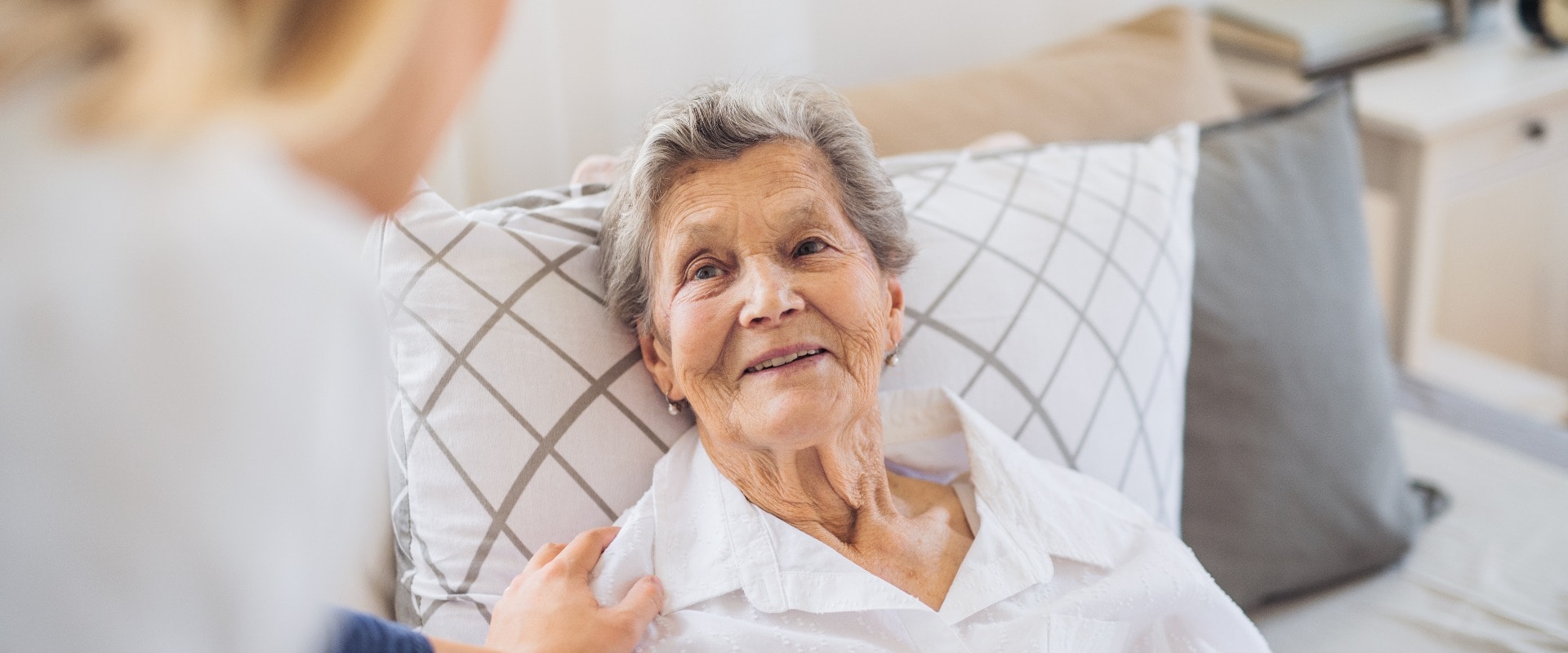 A health visitor talking to a sick senior woman lying in bed at home.